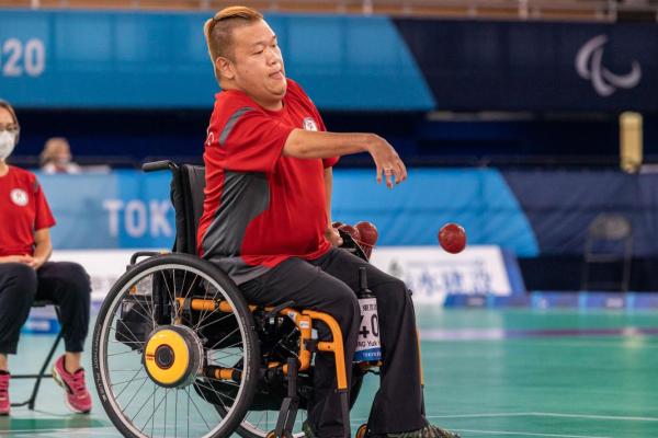 Male wheelchair boccia player throwing red ball
